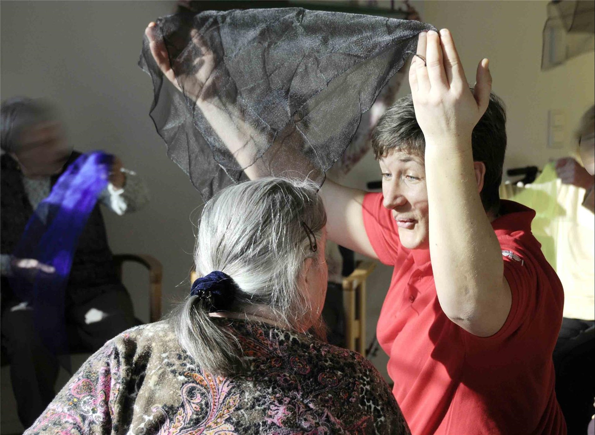 Tagespflege: Frau hebt Tuch in die Luft, davor andere Frau